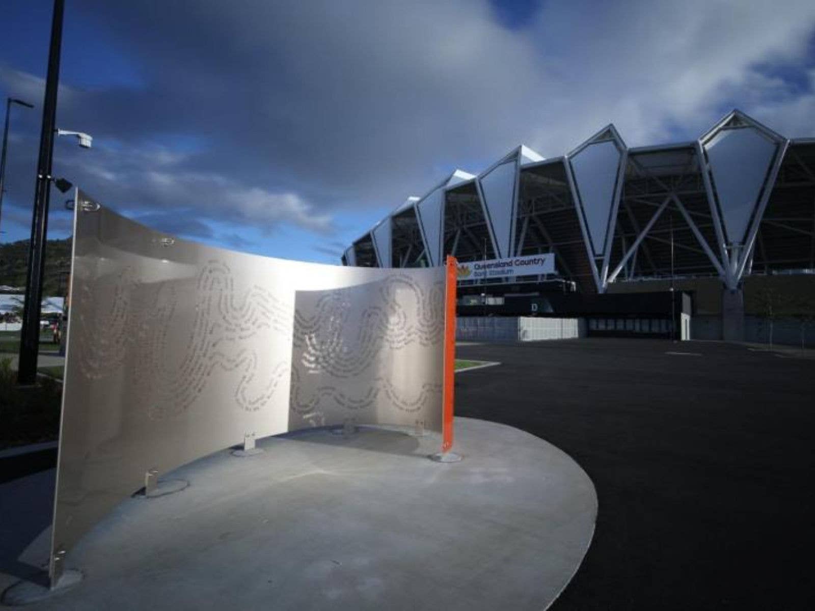 A curved metallic sculpture with etching on the front and orange on the back